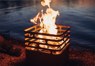 Ein stilvoller Feuerkorb brennt bei Sonnenuntergang am Seeufer – warme Flammen tanzen in einem modernen, kubischen Design aus Metall. Die glühende Atmosphäre lädt ein zu Momenten voller Genuss, Natur und Geselligkeit – genau wie Altawolfs: authentisch, geschmackvoll und mit Charakter. Dieses Bild steht für die Wärme echter Zutaten, das Feuer kreativer Ideen und das Lebensgefühl hinter unseren Gewürzen, Inhalten und Produkten.  Diesen hochwertigen Feuerkorb kannst du direkt in unserem Webshop unter scandinavian-flowers.com kaufen – für stilvolle Outdoor-Abende mit Atmosphäre. 